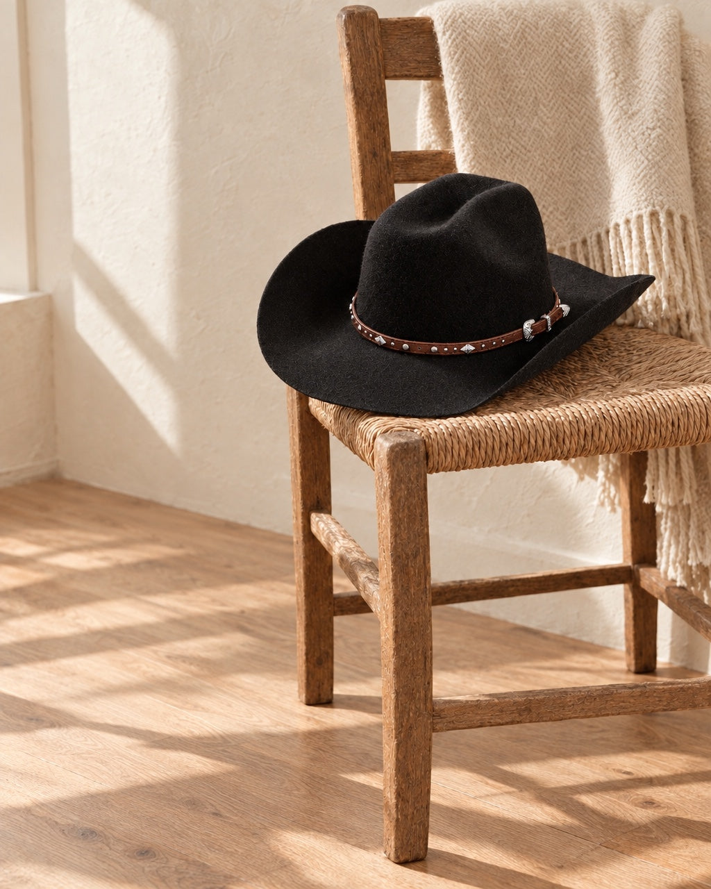 Chapeau cowboy en feutre noir à bande cloutée, posé sur une chaise paillée